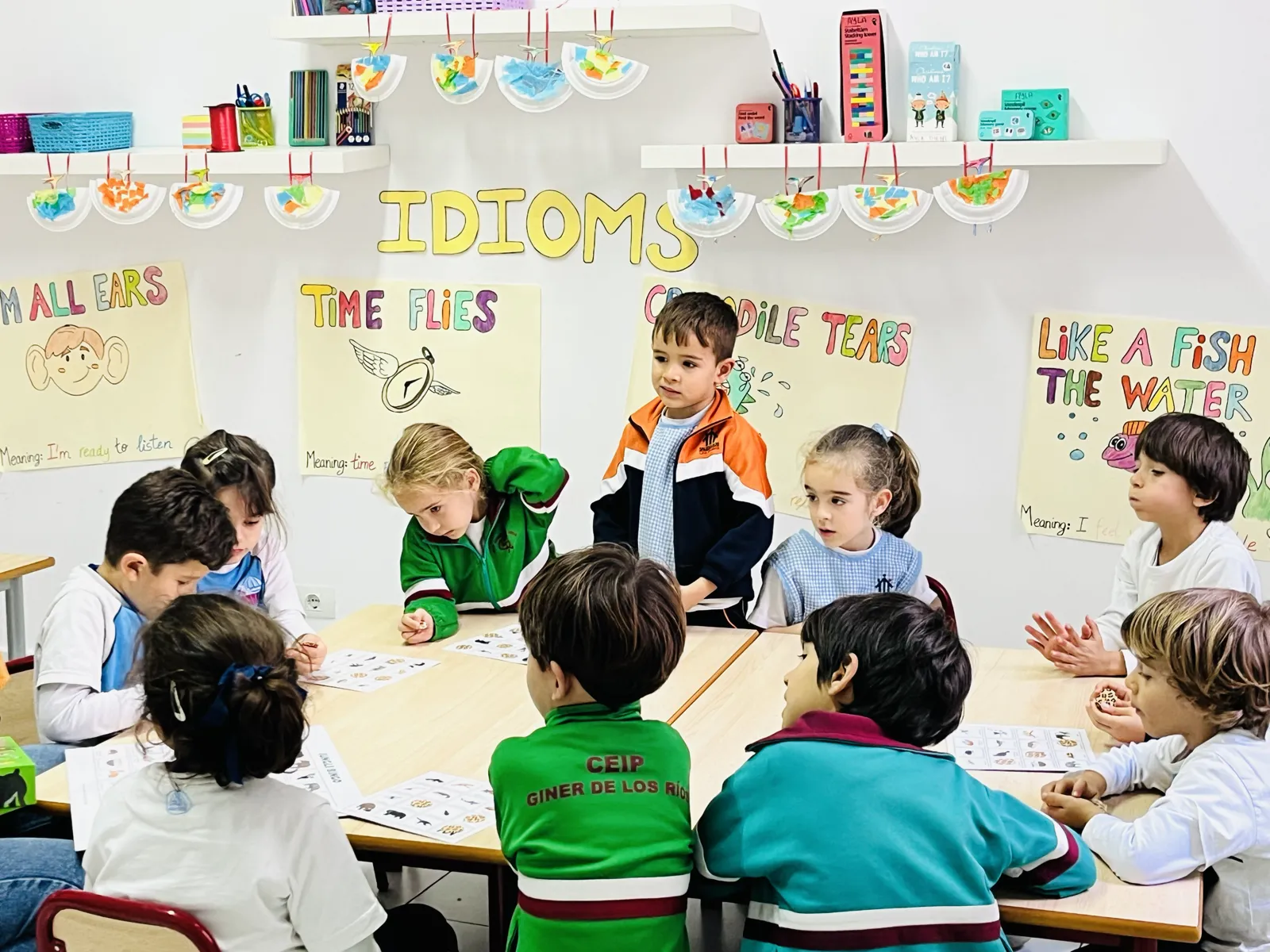 Niños trabajando en grupo alrededor de una mesa con material en inglés